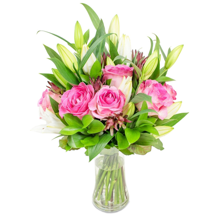 A refined bouquet of lush pink roses and poised white lilies is displayed in a clear glass vase against a stark white background, the presentation intentionally minimal to celebrate form, colour and scent. Several roses are open to show their velvety, layered petals in hues ranging from pale blush to saturated fuchsia, the way each curl and fold catches the light suggesting softness you could almost feel. Interlaced with the roses are white lily buds, some elongated and unopened like quiet promises, others partially open and revealing the smooth trumpet-form and the first hint of fragrance. Surrounding the flowers is a generous volume of greenery: larger pointed, glossy leaves provide structure while finer, paler-green sprigs add movement and soften the silhouette. Subtle, darker reddish-brown accent buds or foliage are distributed through the arrangement to introduce depth and a measured rustic note against the otherwise luminous palette. The glass vase, gently tapered at the base, holds clear water where the carefully trimmed stems are plainly visible, indicating thoughtful preparation and freshness. Bright, even lighting eliminates dramatic shadow, making this bouquet ideal for product imagery, a heartfelt anniversary gift, or as a calming centrepiece for a home near Queensbury's local markets and community spaces. The overall impression is one of considered beauty: fragrant, celebratory, and expertly balanced-an arrangement that feels at home on a windowsill in Queensbury or as a polished surprise delivered to a neighbour on a special day.