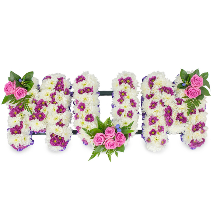 This handcrafted sympathy tribute spells MUM in bold, three-dimensional letters made from a dense carpet of pure white chrysanthemums, their tiny petals combining to form a plush, cloud-like surface that reads as a tactile expression of devotion. Against a pristine white background the letters take on sculptural clarity: subtle pools of deep purple and magenta spray chrysanthemums are thoughtfully placed among the white, creating patterned variation and visual depth. The composition is animated by three pink spray rose bouquets - a restrained cluster at the top left of the first M, a fuller arrangement of several roses tucked into the lower curve of the U, and a matching cluster at the top right of the final M - each bouquet embraced by rich green foliage and delicate fern fronds. Small blue accent flowers appear as gentle punctuation marks, their cool tone balancing the warmer pinks. A delicate purple ribbon edges the silhouettes, refining the form, while an understated dark horizontal bar connects the letters from behind, giving the piece a sense of cohesive structure without detracting from its floral surface. The lighting is gentle and even, emphasising the softness of the chrysanthemums and the layered textures of petals and leaves. As a Queensbury florist familiar with local chapels and community services, I imagine this design placed at a church near the high street or beside a family photograph, an elegant and personal way to honour a mother or matriarch with careful craftsmanship and quiet affection.