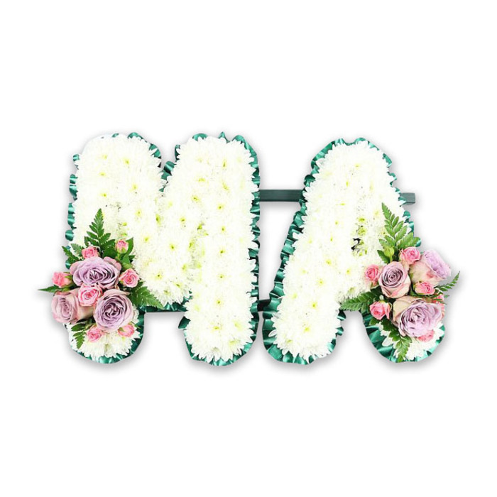This carefully composed floral tribute spells out the capital letters MA, a simple yet deeply personal farewell likely created for a cherished mother or grandmother. Against a bright, neutral white background, every curve and angle of the letters is defined with precision. The body of each letter is densely packed with small, pristine white chrysanthemum heads, arranged so closely together that they form a continuous, cushion-like surface. The flowers' many fine petals add a soft, almost velvety texture, conveying purity and tenderness without feeling stark. Running along the outer contours of both the M and the A is a band of lush emerald satin ribbon, gently ruffled to create a pleated edge. This rich green border brings structure and contrast, framing the white blooms in a way that feels both contemporary and deeply traditional, reminiscent of many tributes delivered to churches and crematoria around Queensbury and the surrounding Harrow area. Where the left leg of the M meets its base and the right leg of the A touches the bottom line, two identical accent arrangements rest like corsages. Each cluster features a gentle blend of lavender-toned and lilac roses, softer blush pink roses, and tiny, tight pink spray rose buds, all nestled together in a small, rounded grouping. A single fern frond in each cluster extends gracefully outward, its feathered leaves adding lightness and a touch of natural movement. The colour palette of white, pink, and lilac, supported by fresh greens, suggests love, remembrance, and quiet gratitude. Composed with evident care and craftsmanship, the tribute feels like something created by a local Queensbury florist who understands how flowers can speak for a family when emotions run high and words are hard to find.