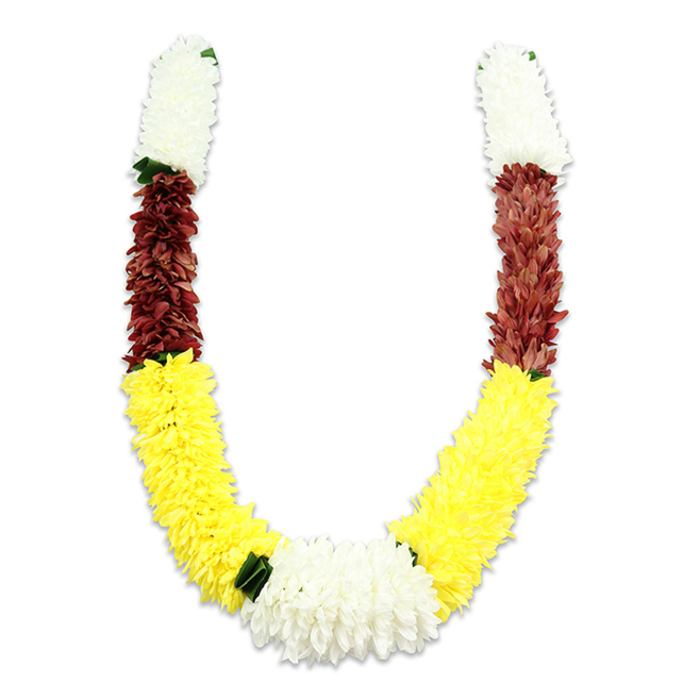 A U-shaped traditional garland photographed on a stark white field so every detail of its construction reads clearly: short, densely clustered cylinders of creamy white blooms begin each arm, their tiny petals layered tightly to create a soft, pillowy top. Beneath those white crowns sits a band of deep maroon or reddish-brown, composed of compact fabric petals that introduce a rich, earthen counterpoint to the lighter tones. The garland then unfurls into extended sections of bright yellow-evocative of marigold strings-where plush, rounded clusters form the sweeping lower curve. At the nadir of the U, a generous, broader mass of pure white, chrysanthemum-like flowers reunites the composition, acting as a visual anchor. Small, dark green leaf-like accents are positioned where colours meet, particularly between the yellows and whites, to soften transitions and suggest a ribbon of foliage between floral segments.
The piece is clearly artificial: thousands of textile petals and carefully stitched cores give it an appearance of abundant freshness while ensuring longevity for ritual use. Seen from the perspective of a local florist working around Queensbury, with customers coming from nearby Kingsbury, Honeypot Lane and Wembley Park for religious celebrations, this garland reads as both ceremonial and practical-designed for repeated use in Hindu puja, temple offerings, weddings and seasonal festivals. Its palette-white for purity, yellow for prosperity, maroon for devotion-remains deeply symbolic, and the workmanship captures the reverence and care typically found in community-made malas.