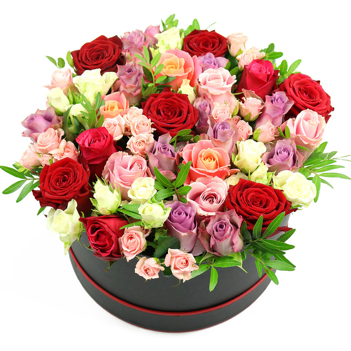 A sophisticated rose hat box arrangement is captured in a studio-style image, perfectly centred against a smooth white background that highlights its luxurious detail. The container is a sleek, cylindrical box in deep black, edged with a narrow band of red trim around the base, echoing the richness of the red roses overflowing from the top. The flowers are arranged in a lush, rounded dome that completely conceals the rim of the box, creating the impression of a cushion of petals resting on a dark plinth. Dominant within this tapestry of blooms are sumptuous crimson and scarlet red roses, their velvety petals layered densely to create dramatic depth and passion. Scattered between them are romantic fuchsia tones, soft blush pink blossoms, and warm coral and peach roses, each petal delicately curving and catching the light. Creamy white and ivory roses punctuate the design, adding brightness, while graceful lavender and muted purple roses introduce a cool, sophisticated note that keeps the palette from becoming too intense. The bouquet includes roses at different stages of openness: some fully unfurled and generous, others half-open, and clusters of smaller spray roses still curled in tight buds, which add intricacy and movement. Fine sprigs of fresh greenery, likely ruscus or similar filler foliage, emerge here and there among the blooms, creating a gentle contrast against the softness of the petals and enhancing the sense of fullness. The overall composition has been crafted with an expert florist's eye, the kind you might expect from a boutique studio serving Queensbury and nearby areas, where residents send such arrangements for anniversaries, birthdays, Valentine's Day, Mother's Day, or any moment deserving a grand, heartfelt gesture. The image conveys not only colour and form but also the feeling of a special delivery arriving at a doorstep on a quiet Queensbury lane.