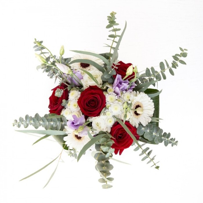 For Queensbury residents seeking a bouquet that captures both subtlety and sophistication, this arrangement reveals layers of intentional detail with every glance. The radiant white gerberas anchor the ensemble, their creamy petals reflecting the spacious light often found in modern Queensbury homes. Meticulously placed among them, rich crimson roses unfurl their spiraled blooms, conveying deep affection and enduring devotion-ideal for anniversaries, sympathy, or heartfelt gestures. Wisps of cool eucalyptus drift above the florals, casting gentle shadows and inviting admiration for the play of texture and light. Lilac lisianthus scattered throughout offer a contemporary twist, each bud suggesting promise and new stories on the horizon. Small, fluffy white filler flowers create a cloud-like halo, while the robust base is lined with glossy, dark foliage that professionally frames the bouquet. Every green stem, cut fresh and submerged in the crystal-clear water of a glass vase, assures both quality and longevity-perfect for same-day delivery across the Queensbury area. The scent is a subtle tapestry: the soft green of eucalyptus, the unmistakable heart of rose, and the crispness of the fresh cut, all reminiscent of Sunday strolls between shops on Queensbury Circle. This composition is crafted for occasions that call for beauty and meaning, each element chosen by a skilled local florist who understands both tradition and modern tastes.