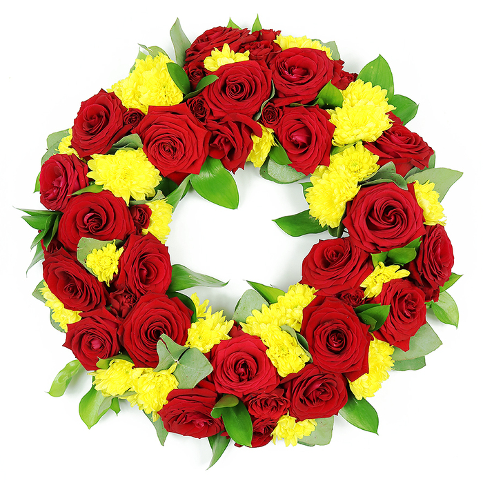 A large, circular sympathy wreath filled edge to edge with red roses and yellow chrysanthemums is presented against a stark white backdrop, allowing every bloom and leaf to be clearly seen, as if laid out in the workroom of a Queensbury florist before delivery. The wreath's structure is robust and full, yet the circle remains clean and precise, forming an unbroken ring with an empty centre that subtly suggests eternity and ongoing remembrance. Dozens of deep red roses form the foundation of the design; they are at the ideal stage of opening, with outer petals just beginning to relax while the inner spirals remain tight and defined. Their velvety petals hold tones from clear crimson to slightly deeper burgundy, creating a play of light and shadow within each flower. Between these roses, clusters of small, joyful yellow chrysanthemums-or button-like spray chrysanthemums-are tucked closely together, their tightly packed, fine petals forming textured spheres that brighten the entire wreath. The yellow blooms soften the emotional weight of the red, bringing a suggestion of gratitude and the celebration of a life well lived. Around and beneath the flowers, a rich mix of foliage provides structure: broad, leathery leaves in a strong, glossy green are interwoven with more delicate, muted green and silvery-green foliage that likely includes eucalyptus, hinting at a fresh, slightly aromatic scent. The high, even lighting ensures that the contrast between the red, yellow, and green is vivid and true to life, with no distracting shadows. This classic, dignified wreath would be fitting for a funeral or memorial service anywhere in Queensbury, whether placed at a local crematorium, church, or resting place near the quieter residential streets off Church Lane, conveying deep affection and respect through traditional colour and form.