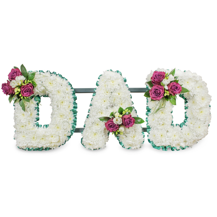 A solemn and lovingly composed funeral tribute spells out DAD in three substantial letters, each formed from a dense sea of small white chrysanthemums whose clustered petals create a soft, voluminous texture that absorbs light and calms the eye. The letters are outlined with a pleated emerald-green ribbon that gives a crisp silhouette and a whisper of formal greenery; its ruffled edge catches subtle highlights, bringing definition without harshness. Placed with deliberate balance, three clusters of deep magenta roses add warmth and personal colour: one on the upper left curve of the first D, another quietly seated in the A's lower center V, and the third on the upper right sweep of the final D. Intermingled with the roses are small white freesia or spray blooms and generous, dark-green foliage, which together create pockets of shadow and fragrance that invite a closer, contemplative look. A low-profile dark green or grey bar supports the letters from behind, indicating a funerary display stand designed for stability at a church, crematorium, or cemetery. As if described by a local Queensbury florist who knows the tone of the area's services, this arrangement combines classic dignity and intimate detail-suitable for a graveside farewell or memorial service, offering families a clear, heartfelt message of love and remembrance in a restrained, tactile design.