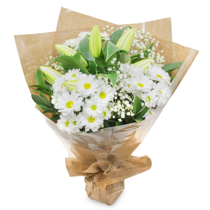 Centered against a pristine white backdrop, this thoughtfully arranged bouquet of white and green blooms exudes quiet grace, reminiscent of a peaceful walk through the residential streets of Queensbury at dusk. The main body of the arrangement is composed of numerous daisy-style white chrysanthemums, their multiple layers of fine, pristine petals forming soft, rounded discs. Each flower has a distinct yellow-green centre that glows like a gentle light, adding a touch of warmth to the cool white palette. Interwoven among these daisies are several tall lily buds, their long forms still firmly closed, shaded in light green with subtle creamy hints at the tips where the petals meet. The lilies' upward tilt brings elegance and a sense of unfolding chapters, making them an especially poignant feature for a sympathy bouquet. Sprinkled delicately throughout, clouds of white baby's breath create a gossamer veil, their tiny blossoms softening the borders and adding a sense of lightness and space. Around the perimeter, lush dark green leaves arch and overlap, providing a rich, verdant framework that makes the white blooms appear even more luminous. The florist has wrapped the stems in a layer of rustic brown kraft paper, its natural texture and warm tone evoking the feel of local Queensbury markets and independent shops. Over this sits a protective layer of clear, slightly crinkled cellophane that catches the light and keeps the arrangement pristine for delivery. Neatly gathered and tied at the base, the bouquet feels ready to be carried to a memorial service, laid beside a photograph, or placed in a vase at home as a tender reminder of love, comfort, and enduring memories in the Queensbury community.