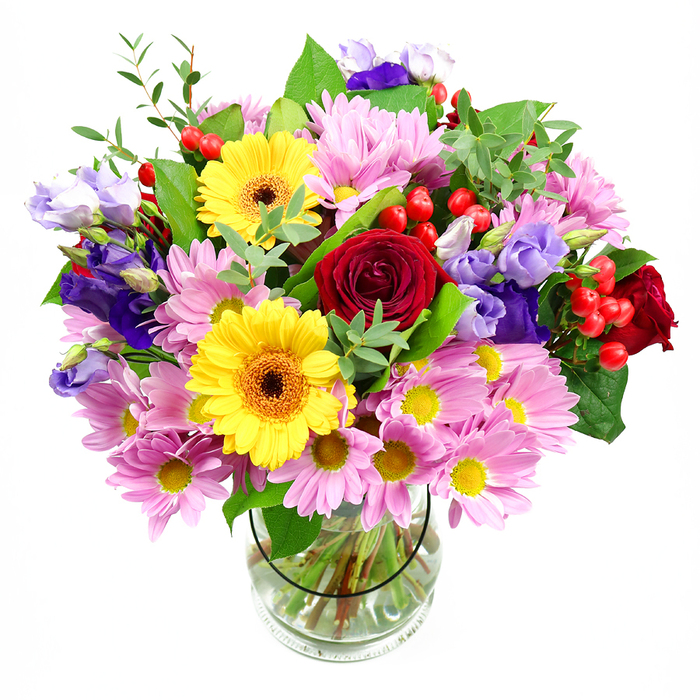In this image, a lush mixed bouquet is presented in a simple clear glass vase, set against a white background that allows the colours to sing, much like flowers catching the light in a Queensbury townhouse window. At its core, luxurious deep red roses open in layered spirals, their velvety petals suggesting warmth, devotion, and a touch of classic romance. Flanking them are bright yellow gerbera daisies, each bloom centred with a distinctive brownish-orange eye that adds depth and draws the gaze, like small suns anchoring the arrangement. Surrounding this central cluster, soft pink and lavender daisies or chrysanthemums spread generously, their multi-petalled heads and tiny yellow centres creating a cushion of gentle colour and texture. Scattered gracefully through the bouquet are elegant purple and lilac lisianthus blooms, their bell-shaped, slightly ruffled petals introducing a cool, refined note that balances the cheerfulness of the daisies and gerberas. Glossy red Hypericum berries peep out between petals and leaves, tiny spheres of colour that add a playful, almost festive feel. Layers of green foliage-from broad, dark, shiny leaves to lighter, more delicate stems-frame and support the flowers, giving the design natural fullness and movement, as if freshly gathered from a garden near Queensbury Circle. The clear vase reveals carefully trimmed stems arranged in a neat fan and submerged in clean water, reflecting professional care and freshness. This bouquet feels ready for a joyful celebration, whether it's a birthday, an anniversary dinner at home, or a thoughtful same-day surprise delivery to someone special in and around Queensbury.
