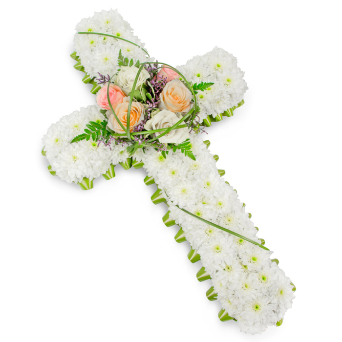 A solemn yet comforting floral cross, traditionally associated with Christian funerals, is displayed on a pure white background that allows every detail to stand out with clarity. The entire structure of the cross is built from countless petite white chrysanthemums or similar clustered blooms, placed so tightly that no gaps are visible. This dense blanket of white flowers creates a plush, almost quilted texture, evoking purity, peace, and quiet reflection. Around the outer edge of the cross, a defined ribbon of fresh green foliage forms a living frame, lending a crisp outline to the arms and the base, much like the well-kept hedges and lawns you might notice when walking through the quieter residential streets of Queensbury. At the intersection of the cross, a slightly elevated central spray becomes the emotional focal point. Here, several roses in soft, warm shades-gentle peach, muted coral, and creamy ivory-open in layered spirals, their colour echoing the tenderness of cherished memories. They are nestled among delicate fern fronds, fine blades of grass that curve gracefully over the blooms, and tiny purple filler flowers that introduce a subtle touch of cool tone without overpowering the serene palette. The lighting is neutral and balanced, revealing the natural sheen of the rose petals and the matte softness of the chrysanthemums, while casting only the faintest of shadows beneath the blooms. This floral cross, likely created for a funeral or memorial service in or around Queensbury, feels deeply respectful and heartfelt, a quiet testament to faith, love, and eternal rest, designed to offer comfort to grieving families through its understated beauty.