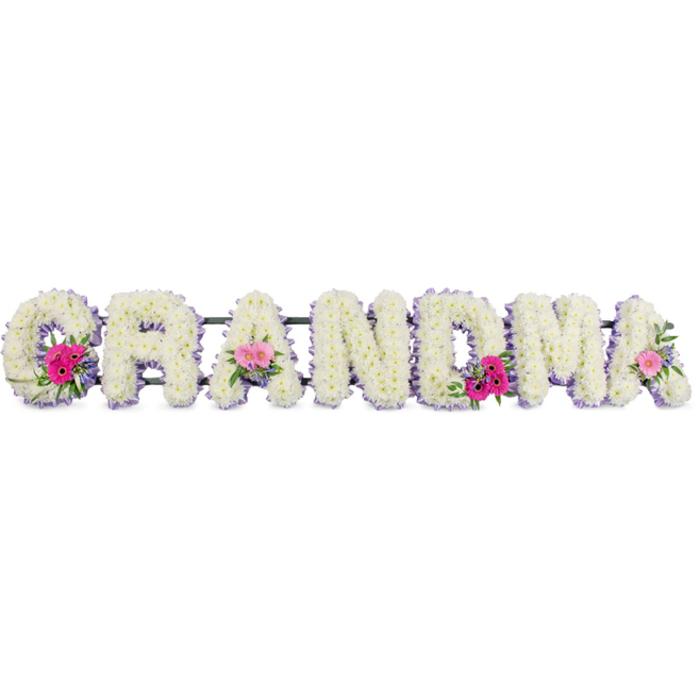 In this tender funeral display, the word GRANDMA is beautifully written in flowers, each letter shaped on a padded base and entirely covered with white chrysanthemums. The blooms are small, neat, and tightly packed, creating a richly textured surface like a soft quilt of petals. Tiny yellow-green centres are barely visible, giving just a hint of warmth within the blanket of white. A slim lilac ribbon runs along the outer contours of each letter, its gentle purple tone adding a touch of calm refinement, almost like a halo surrounding the tribute. At three points along the word, delicate accent sprays bring gentle colour: at the start of the G, at the centre A, and at the final A, clusters of flowers nestle into the chrysanthemums. These sprays feature bright yet tender pink gerbera daisies with evenly spaced petals, alongside blushing pink roses opening in layered spirals, interwoven with sprigs of fresh greenery that fan out lightly, softening the edges of the letters. The image is lit with diffused, studio-style light, which keeps the whites crisp but not harsh, allowing the lilac and pink tones to remain soft and soothing. The overall impression is calm, respectful, and affectionate, exactly the kind of tribute a family in Queensbury might choose when gathering at a local church or crematorium to honour their grandmother's life. One can almost imagine the subtle floral scent lingering in the air-clean chrysanthemums and mild rose-offering quiet comfort amid the sadness. This arrangement captures a balance between formality and warmth, visually expressing love, remembrance, and the gentle dignity of a farewell shared with close family.