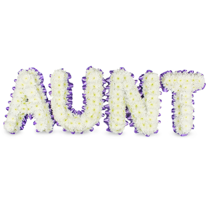 A meticulously crafted sympathy tribute spells AUNT in four large capital letters, the surface of each letter formed from hundreds of small, immaculate white spray chrysanthemums. The dense packing of the blooms creates a plush, cloudlike texture; individual florets display faint pale-yellow centres that bring a whisper of warmth into the predominantly white composition. Each letter is edged with a vivid purple satin ribbon that has been worked into a soft ruffle along the perimeter, creating a scalloped frame that contrasts with the creamy petals and accentuates the letter shapes. The ribbon's satiny shine and subtle pleating give tactile depth and a considered finish as it traces every curve and angle of the underlying frame. Under soft studio light, thin grey shadows appear beneath each letter, revealing their three-dimensional frames and the breathing space between the pieces-intended to read well from a distance, whether placed in a church nave, crematorium chapel or family lounge. There is a discreet, green floral fragrance-fresh, clean and slightly dewy-from the chrysanthemums, lending the tribute a gentle presence rather than heaviness. This composition reads as a personal, reverent memorial designed to honour a cherished aunt; local floral professionals serving Queensbury and neighbouring Harrow and Wembley would describe it as a dignified, bespoke statement of remembrance, crafted to offer comfort through thoughtful colour, texture and precise workmanship during a time of loss.