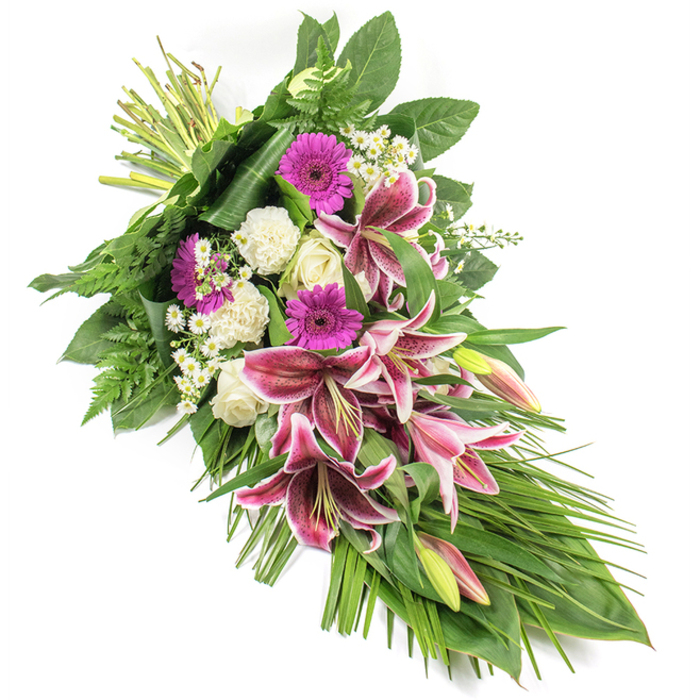 A beautifully composed funeral spray, photographed clearly against a stark white background, stretches in an elegant diagonal from the top left to the bottom right, creating a soft teardrop shape that conveys both movement and calm. The focal point is a cluster of dramatic Stargazer lilies, their broad petals glowing in intense fuchsia-pink, edged delicately in white and patterned with burgundy speckles, like brushstrokes on silk. Some of the lilies are fully open, revealing their pollen-tipped stamens, while others remain in green and pink buds, suggesting unfolding memories and continuing love. Nestled among them are creamy white roses, some tightly furled and others just beginning to spiral open, symbolizing respect and gentleness. Ruffled white carnations add volume and a cloud-like softness, embracing the more vibrant blooms. Bright magenta gerbera daisies are carefully interspersed, their flat, daisy-shaped faces bringing touches of joyful colour that temper the solemnity. Throughout the arrangement, fine clusters of tiny white daisy-like filler flowers lighten the palette and draw the eye along the length of the spray. Surrounding all the blooms is an abundance of lush greenery: broad, glossy dark leaves create a firm, structured base, feathery ferns lend delicate texture, and slender, arching grass-like leaves extend gracefully downward, reinforcing the cascading form. The stems at the top left are securely bound, showing skilled, hand-crafted work reminiscent of a local Queensbury florist preparing flowers for a chapel on Church Lane or a quiet home service. The overall impression is of a respectful, heartfelt tribute, ideal for expressing sympathy and honouring a life with beauty and dignity.
