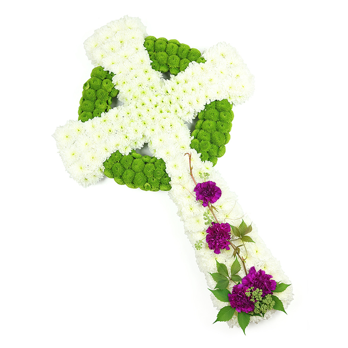 In this thoughtfully composed funeral image, a Celtic cross made from fresh flowers is set against a spotless white background, drawing full attention to the artistry and symbolism of the tribute. The vertical and horizontal arms of the cross are constructed from compact, snow-white chrysanthemum heads, arranged so closely that they form a padded, cloud-like texture with a gentle dome. Threading through this white foundation is the powerful Celtic design, rendered in bright lime-green button chrysanthemums that delineate the circular ring and intricate interweaving lines. These small spherical blooms add structure and clarity, standing proud against the white and giving the piece a sculptural quality. The cross appears slightly angled, enhancing its three-dimensional presence and highlighting the precision of the ring intersecting the arms. On the lower part of the vertical arm, three separate clusters of luxurious deep purple carnations provide a striking counterpoint. Their rich, velvety petals are gathered in rounded groups that nestle into the white chrysanthemum base, surrounded by strands of dark green foliage and slender, woody trails that curl naturally along the design. This touch of greenery introduces a sense of gentle movement, like a soft breeze through leaves. The overall palette of white, green, and purple conveys purity, renewal, and heartfelt sorrow in equal measure. Created by an experienced florist serving families in Queensbury and the surrounding area, this type of Celtic cross would be a fitting tribute at a church service or crematorium near Queensbury Park, offering a meaningful way to honour Irish or Scottish roots or simply to express steadfast faith and loving remembrance.