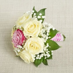 Imagine the gentle hush of a Queensbury morning, where this bouquet-cradled on soft, neutral-hued fabric-whispers of new beginnings and quiet joy. The arrangement's heart is a constellation of pale ivory roses, their petals artfully unfurled, encircling a single vivid magenta-pink rose whose vibrancy mirrors the colourful community spirit found near Honeypot Lane. Wisps of tiny white baby's breath float amidst the blooms, creating a cloud-like halo that lifts the eye and spirit alike. Shadows and light dance across the bouquet, accentuating the texture of velvety petals and glossy green leaves, suggestive of the lush gardens found in nearby local parks. The stems are tightly bound in a gleaming pink satin ribbon spiraled with petite pearls-a modern flourish infusing timeless craftsmanship, perfect for an elegant Queensbury wedding or an intimate celebration at home. The entire arrangement radiates tenderness, artistry, and fresh-picked vibrancy, offering a sensory impression of gentle rose scent mingled with greenery. Designed with thoughtful detail by a seasoned Queensbury florist, this bouquet is more than flowers-it's a poetic gesture of love and celebration, rooted in community and lasting memories.