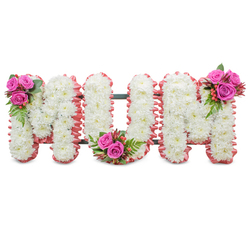 There is a quiet dignity to this funeral tribute that spells "MUM" in large, connected block letters, set starkly against a white backdrop so each floral detail is visible. The core of every letter is tightly filled with pristine white chrysanthemums - small, dense blooms whose layered petals create a soft, cushion-like texture that reads as purity and calm. A ruffled, pale pink ribbon traces the outer contour of each letter, lending a gentle, motherly softness to the design and a warm contrast to the white. Visible between the letter forms is a dark green structural frame, the discreet skeleton that keeps the tribute upright at a service or graveside. Three concentrated posies of rich fuchsia-pink roses punctuate the composition: one at the shoulder of the first M, one cradled at the base curve of the U, and one on the shoulder of the final M. Each cluster is finished with ferny green foliage and small reddish-orange hypericum berries, introducing glossy texture and a complementary colour flash. The overall scent is muted and comforting - the clean earthiness of the chrysanthemums undercut by the soft sweetness of roses. As someone who makes tributes for families across Queensbury, Kingsbury and nearby Wembley, I assemble pieces like this to honour a mother's memory with restraint and affection. Prepared with steady hands and respect, it offers a dignified farewell that looks equally at home inside a chapel on Queensbury Parade or at a graveside service in the local cemetery.