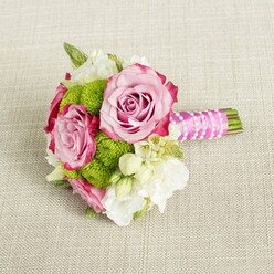 Resting gracefully on a light beige, woven fabric that resembles a linen runner on a Queensbury dining table, this compact bouquet feels like a moment of calm before a celebration begins. Three pink roses, fully opened yet still gently cupped, form the heart of the arrangement. Each rose shows a subtle gradation of colour, with blush pink centres that deepen to rich, almost magenta edges on the outermost petals, giving the illusion of hand-painted watercolour. Between the roses, tidy clusters of lime green button chrysanthemums create bright, rounded cushions of texture, their countless tiny florets forming a cheerful contrast against the soft, romantic roses. Interlaced throughout are delicate white and cream flowers-likely lisianthus or freesia-whose trumpet-like blooms and silky, layered petals soften the composition, bringing a sense of purity and light that would suit a civil ceremony at Queensbury's nearby registry venues. Fine, starry white blossoms with pinpoint yellow eyes, reminiscent of wax flower, add dainty detail at the edges of the bouquet, inviting the eye to linger on each tiny element. The stems are gathered into a short, hand-tied handle, meticulously wrapped in bright fuchsia satin ribbon that catches the light with a gentle sheen. A slender string of white faux pearls winds diagonally over the ribbon, as if draped by a careful florist's hand, lending a classic bridal touch. Beyond the wrap, the green stems appear neatly trimmed and clean. The lighting is soft and even, without glare, enhancing the freshness of the petals and the vivid green mums. The overall mood is romantic yet modern, an intimate posy perfect for a bridesmaid walking through Queensbury streets to an afternoon wedding or engagement celebration.