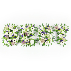 An intimate, handcrafted tribute captured from above, the letters DAD formed in a tapestry of whites, soft purples, and fresh greens that feel both soothing and reverent. Each of the three letters is densely composed: velvety chrysanthemums and full ivory gerberas create broad, luminous surfaces while pastel coffee-toned roses and creamy white lisianthus add quiet sophistication and warmth. Ruffled carnations in soft mauve and lavender introduce a gentle ripple of texture, and sprigs of deep violet statice or similar filler flowers bring small, respectful accents that catch the eye without demanding attention. The perimeter of each letter is lined with lively fern leaves whose crisp, serrated edges frame the petals and introduce a sense of natural movement; compact green button chrysanthemums are tucked throughout, offering contrast and a fresh, garden-like depth. A dark grey structural backing subtly shapes the letters and peeks through here and there, ensuring clarity when the tribute is displayed on a chapel stand or near a crematorium at a funeral service. The overall impression is calm, consoling, and meticulously arranged - the soft scent of white blooms mingling with green foliage like a quiet embrace. Thoughtfully suited for memorials in Queensbury and neighbouring areas such as Kingsbury and North Harrow, this floral DAD tribute speaks of steady love and remembrance, a tangible expression for those who want to honour a father with dignity and tender craftsmanship.
