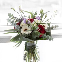 Bathed in the gentle daylight that filters through many Queensbury kitchens, this stylish floral bouquet strikes a perfect balance of colour and grace. Deep, velvety red roses stand proudly at the center, their lush petals layered like the pages of cherished memories. Crisp white gerbera daisies open wide beside them, their espresso centres mirroring the welcoming warmth found in the cafés along Honeypot Lane. Slender stems of pastel lisianthus-some still unfurling-twine thoughtfully throughout the arrangement, hinting at fresh beginnings and quiet transformations. Eucalyptus, with its cool, silvery-green discs, weaves between blossoms, arching softly to envelope the brighter hues and adding a whisper of aromatic greenery. Gathered in a transparent vase that displays each stem's healthy strength, the bouquet also features trailing ivory filler flowers that cluster like morning clouds. Robust, emerald leaves cradle the base, giving the composition a polished, contemporary feel. As the fragrance drifts-a mix of sweet rose and invigorating eucalyptus-it transports you to a dewy morning in Roe Green Park. Perfect for marking special occasions or simply bringing a breath of local freshness indoors, this arrangement from a trusted Queensbury florist is designed to foster connection and share natural beauty with every delivery.