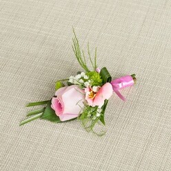 Bathed in soft morning light across a textured backdrop reminiscent of traditional Queensbury linens, this bespoke boutonniere whispers of romance and attention to detail. The focal bloom, a delicate pale pink rose, offers a visual narrative of new beginnings with petals spiraling inward, each layer gently transitioning from a glowing pink core to the palest blush at its rim. Accompanying the rose, a captivating peachy-pink Alstroemeria, possibly sourced from nearby Edgware florists, opens to reveal subtle yellow streaks and brushstroke markings that mimic the gentle complexity of nature. Clouds of baby's breath float throughout the design, creating an airy softness, while pin-sized green mums pack a lively, textural punch, drawing the eye in with their intricate form. Surrounding foliage-spiky dark green grass, airy ferns, and deeper leaves folded with craftsmanship-grounds the accessory, recalling Queensbury's leafy avenues and green spaces. Binding the composition is a bold, fuchsia satin ribbon knotted in a tidy bow, its sheen a subtle nod to celebration. The entire arrangement feels infused with the spirit of joyful local gatherings, perfect for weddings or special events where every minute detail matters. The neutral linen underlay, woven with character, allows the boutonniere's shades to glow, turning it into a poetic accessory for a groom, usher, or guest seeking a touch of Queensbury elegance on a memorable day.