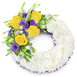 A meticulously made circular funeral wreath, photographed on a plain white backdrop, where the majority of the ring is a plush blanket of tiny white spray chrysanthemums tightly clustered to present a serene, cloud-like surface. The chrysanthemum heads form a continuous, velvety texture that refracts soft light and conveys purity and solemnity. From the upper left quadrant a striking floral spray arcs gracefully across the top: rich yellow roses, fully unfurled in warm butter-gold tones, offer a gentle, comforting presence; mingled with them are deep purple lisianthus (Eustoma) whose satin, ruffled cups provide dignified contrast and a cool visual counterpoint. Several unopened Eustoma buds in soft lavender and pale green lend natural movement and the promise of unfolding. Interspersed foliage - glossy, rounded leaves with faint variegation, delicate fern-like fronds, and slender sprigs - gives structure and grounds the colours, enhancing the freshness of the blooms. A subtle dark purple mesh trim peeks beneath the chrysanthemum base along the inner and outer circle, a refined detail that ties the accent cluster into the whole design. The overall effect is respectful, calm, and beautifully balanced - an arrangement we craft at Flower Delivery Queensbury for families across Queensbury, Kingsbury and Wembley who want a tranquil expression of sympathy. The wreath's texture, tones, and muted scent make it suitable for chapel tributes, memorial services, or as a comforting display at home.