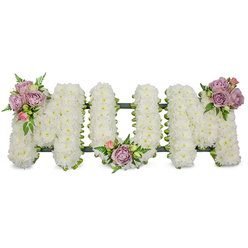 An elegant sympathy tribute arranged in large, three-dimensional letters reads "MUM", each letter constructed from a dense mass of pristine white chrysanthemums that create a soft, textured surface reminiscent of freshly fallen snow. The overall effect is one of serene purity: the white blooms reflect a subdued light and form a calm backdrop for three artful accents - small clusters of soft lavender roses and pale pink rosebuds placed with intention on the upper left of the first M, tucked into the central curve of the U, and crowning the upper right of the final M. Bright green foliage, including delicate fern fronds and lighter green leaves, threads between the pastel roses and the chrysanthemums, adding contrast, movement, and the reassuring freshness of living stems. A dark green structural base, visible along the bottom edge, provides a subtle outline and support so the letters stand with dignity. The roses lend a velvety scent that mingles with the clean, faint scent of the chrysanthemums; together they convey sympathy, respect, and warmth. This arrangement feels hand-finished by an experienced Queensbury florist who understands local funerals and wakes - suitable for a chapel service or graveside near Kingsbury High Road or the quieter corners around Wembley - and it arrives as a composed, heartfelt message of remembrance and love in a difficult time.