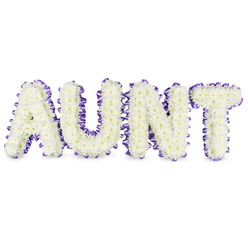 Carefully assembled in a small Queensbury studio close to the station, this personalised memorial piece spells "AUNT" in four bold, elegant letters, each densely packed with pristine white spray chrysanthemums. The chrysanthemums form a textured, cloud-like surface; their profusion of small petals softens the strong letterforms while tiny pale-yellow centres add the smallest, warm accents that catch soft daylight. Around every letter, a deep purple satin ribbon has been worked into a ruffled outline, the ribbon hugging curves and corners with neat pleats that frame the whiteness and lend the tribute a refined, finished silhouette. Grey shadowing beneath the letters reveals the depth of the frames and suggests the solid, three-dimensional construction of the display-designed to sit upright at a service, chapel or memorial table. A gentle green, floral scent arises from the chrysanthemums: clean and slightly dewy, calming for those nearby. The palette of white and purple reads as classic sympathy colouration-white for purity and remembrance, purple for dignity and heartfelt respect-so the arrangement feels like a dignified farewell. Prepared by experienced hands familiar with Queensbury, Kingsbury and nearby Wembley, this bespoke memorial is intended to communicate love, gratitude and the distinct place a beloved aunt held in family life, available as a considered tribute for wakes, funeral services or a quiet home remembrance.