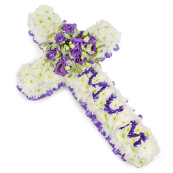 This carefully crafted Christian cross reads as a quiet statement of remembrance: a dense field of pristine white chrysanthemums forms the main surface, petal upon petal arranged to give a soft, cloud-like texture that speaks of peace. A pleated ribbon of deep purple satin traces the entire perimeter, its ruffle adding an elegant silhouette and a subtle contrast that catches the light in gentle folds. Down the vertical shaft, the word "MUM" is spelled out in compact purple blooms-likely lisianthus or small spray chrysanthemums-each tiny flower chosen for colour uniformity so the dedication stands out crisply against the white background. At the heart of the cross a concentrated spray becomes the focal point: rich violet roses with tightly furled buds, softer lavender eustoma or lisianthus, and variegated green foliage with pale edges that highlight the floral masses. Tiny green berries or seeded accents provide a tactile counterpoint, while the overall scent is a faint, clean rose-and-green aroma that comforts without overwhelming. Crafted with the care I give every sympathy commission in Queensbury, this tribute feels suitable for chapel services, wakes, or a graveside farewell in the local area of Queensbury, Harrow and nearby Kingsbury, and is available for thoughtful local delivery through Flower Delivery Queensbury for families seeking a personal, dignified expression of loss.