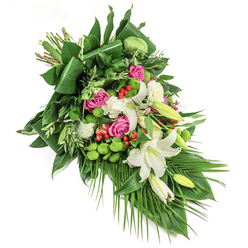 A dignified and lush cascading arrangement, arranged diagonally across a stark white backdrop, that moves like a gentle current of comfort and remembrance. Dominant white oriental lilies anchor the design - their broad, creamy petals and exposed pale-yellow stamens giving a sense of purity and calm; some lilies are fully open and fragrant in spirit, while others remain as tender buds, signifying memory and quiet hope. Warmth is introduced through groups of vivid pink and fuchsia roses, whose velvet layers soften the composition and provide a human tenderness. Interspersed are small white spray carnations, their ruffled faces adding softness and density, while clusters of chartreuse santini chrysanthemums offer a lively, almost cushion-like texture, brightening the composition without overwhelming its serenity. Dotted among the blooms, small red hypericum berries act as gentle accents, their glossy roundness creating pleasing visual punctuation. The greenery is plentiful and varied: large glossy leaves folded into elegant lines form a deep foundation, while lighter, airy foliage and long palm fronds cascade downward to the right, enhancing the sense of movement. Light plays off the satin petals and the sheen of the foliage in a restrained morning glow, emphasizing depth and form. This arrangement reads as a carefully considered tribute, appropriate for memorials and funerals, and carries the quiet professionalism of a Queensbury florist who understands services and families in the local Kingsbury and Wembley communities.