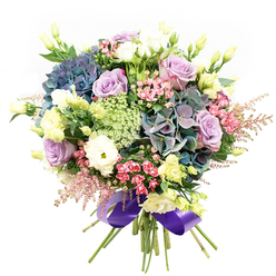A lavish and thoughtfully arranged bouquet unfolds like a floral tapestry, its intricacy echoing the vibrant diversity found throughout Queensbury's neighborhoods. At its heart, voluminous hydrangeas in shades of dusky blue, teal, and soft purple provide rich stones of colour and texture, their plush petals forming a dramatic focal point reminiscent of flower markets near Kingsbury Road. Among them nestle elegant roses; soft lavender and creamy white blooms emerge in graceful spirals, radiating a sense of gentle romance and calm. Tightly clustered white ranunculus introduce a ruffled softness, while tall stems of pale yellow lisianthus add both height and a fresh, airy lightness, much like the spring wildflowers seen on leisurely walks through Queensbury Park. Sprays of vivid fuchsia-pink flowers thread bright, joyful notes throughout the arrangement, and feathery pink astilbe create whimsical, floating accents that lift the bouquet's edges. Filler flowers in translucent greens and whites, possibly Ammi Majus, weave in intricate patterns, lending layers of depth and a delicate balance alongside glossy, deep green foliage. The entire bouquet is expertly gathered and wrapped with a wide, lustrous royal purple ribbon at its base, giving a polished finish that draws together all the cool, soothing hues. Radiating warmth and expert florist craftsmanship, this bouquet conjures both the excitement of celebration and the serenity of thoughtful gestures, making it a perfect centerpiece or a memorable gift, available for delivery across Queensbury and surrounding local streets.