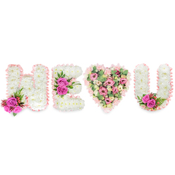 Set against a clean white backdrop, this bespoke floral tribute reads H E (heart) U in a composition that balances quiet dignity with warm affection. The three block letters H, E and U are formed from compact, snow-white chrysanthemums, their dense surfaces creating a soft, clouded effect that suggests peace and purity. Each letter is bordered by a pleated blush-pink satin ribbon, the gentle sheen of the ribbon catching light like a soft ribboned caress. At thoughtful anchor points a trio of vivid fuchsia roses introduces a flash of joyful colour: one cluster settles at the left leg of the H, another crowns the middle bar of the E, and a final pair nestles into the inner curve of the U. These roses are set among deep green, fern-like foliage and tiny reddish-pink berries, adding contrast in both texture and tone. Where a single vertical letter would stand, a full heart replaces it: a lush patchwork of pale pink carnations, delicate lisianthus or small roses, and cooling sprays of pale green eucalyptus, all densely packed to create a romantic, tactile surface. The eucalyptus softens the palette while lending a faint, fresh scent that frames the pink blooms. The recurring blush satin trim unifies the set, a deliberate finishing touch a local florist might choose for a Queensbury service or a personal tribute delivered near Queensbury station and across nearby Wembley and Kingsbury. Flower Delivery Queensbury assembled the arrangement with careful attention to balance, scent and sentiment, producing a piece that both reads clearly at a distance and rewards close inspection.