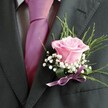 Evoking the spirit of joyful celebrations that bring Queensbury neighbours together, this finely crafted boutonniere is a little poem in petal and stem. At its heart, a blush-pink rose opens gracefully, velvet petals softly spiraling in a way that feels alive with anticipation and new beginnings-perfect for weddings or special events along Beverley Drive. The rose's subtle scent is a gentle presence, promising quiet memories in the making. Around it, baby's breath forms a halo of white-their faintly ruffled blooms imbuing the piece with a lightness like early morning mist drifting across local greens. Slender, fresh foliage arches outwards, their cool greens providing a hint of wildness, grounding the arrangement's classic roots in the natural beauty of Queensbury. This artistry is gathered at the lapel by a lilac satin ribbon, its silky finish glinting softly against the midnight charcoal of the suit. Completed by a vibrant fuchsia tie and crisp pale grey shirt, the buttonhole becomes both a visual and tactile highlight. As a local florist, curating such details means blending tradition and personal stories-each boutonniere a fragrant witness to promises exchanged and milestones celebrated in the heart of Queensbury.