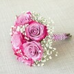 A radiant hand-tied bouquet designed for elegant occasions in Queensbury, this arrangement features a compact, romantic cluster of approximately five roses, each bloom boasting two-toned petals-soft lavender and gentle pink at their core, deepening dramatically to fuchsia and magenta at their outermost edges. Interwoven with fine clusters of pure white baby's breath, the bouquet achieves visual harmony and an airy, cloud-like texture that echoes the freshness of seasonal blooms found near Honeypot Lane. Expertly bound with a deep purple satin ribbon, the handle is further embellished with gleaming strands of white pearls, spiralling gracefully to provide a luxurious and tactile finish reminiscent of local Queensbury wedding traditions. The stems, freshly trimmed and left visible beneath the wrap, signal natural beauty and artisanal attention. Presented diagonally across a pale linen or off-white textured cloth, the ensemble evokes a warm sense of celebration and timeless romance, making it an ideal choice for a bridal party, intimate anniversary, or cherished wedding moment in Queensbury. The arrangement invites memories of joyful gatherings, fragrant gardens, and handcrafted elegance, reflecting a perfect marriage of modern design and classic floral tradition.