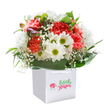 There's an unmistakable joy radiating from this expertly crafted bouquet, its colours and shapes singing with the optimism so often felt during early spring in Queensbury. Immersed within a crisp, square white gift bag, a chorus of coral and ruby carnations unfolds, their delicately ruffled petals spilling out in exuberant waves. Playful white daisies accented with golden-green eyes stand tall beside the carnations, their presence adding cheerful charm reminiscent of weekend mornings at Roe Green Park. Gentle sprays of tiny white baby's breath drift through the arrangement, their dainty clusters lightening the overall look and evoking a sense of innocence and breeziness. Sprightly green leaves, broad and reflective, cradle the blooms, forming a lush backdrop that feels both sophisticated and inviting. On the left, a hint of unopened, purple-tinged buds peeks through-just enough to add mystery and promise. The flowers are gathered with precision, creating a full, rounded silhouette that communicates expert skill and authentic care. Topping the bag, sturdy white ribbon handles promise easy delivery-perhaps soon to a lucky home along Kenton Road. Bathed in gentle light and set against an immaculate white background, the bouquet's vivid colours and textures are amplified, making it a beacon of freshness and delight. Every element-fragrance, texture, composition-speaks to the mastery of a true Queensbury florist, ready to bring a touch of happiness to life's special moments.