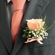 This boutonniere reads like a small poem of celebration, centered on a flawless peach rose whose petals melt from creamy blush at the edges to a warm coral heart. The rose rests with assured grace on a charcoal lapel, its velvet surface catching the light and deepening the colour of the accompanying soft pink tie. Encircling the bloom, delicate sprays of white gypsophila create a cloud-like frame, their tiny blooms bringing an airy, innocent contrast to the rose's rich texture. Slim lengths of fine green foliage and a gently curled support leaf lend structure and a whisper of wildness, the greens bright and dewy as if cut that morning from a Kenton or Kingsbury garden. A small satin ribbon, closely matched in tone to the tie, ties the stems into a polished bow - a florist's signature of care and precision. There's a faint, sweet scent that seems to promise new beginnings: a subtle rose perfume lifted by fresh green notes. Crafted with the sensibility of a neighbourhood florist, this boutonniere would be at home on a wedding suit at a local venue or an intimate anniversary dinner - and at Flower Delivery Queensbury we often prepare pieces like this for same-day requests across Queensbury, Kingsbury, and the Brent area, ensuring each pin is delivered fresh and ready to make its moment special.