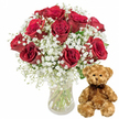 A peaceful, studio-style scene shows a beloved romantic gift combination, crafted with the care of a neighbourhood florist who knows Queensbury celebrations well. On the left stands a clear glass vase holding a generous bouquet of around a dozen deep red roses, each bloom rich with velvety petals that layer tightly at the centre and open gracefully at the edges. The roses vary slightly in size and openness, giving the arrangement a natural, garden-fresh character that feels at home in living rooms near Queensbury Underground or along Cumberland Road. Interlaced between the intense crimson roses are ample sprays of white baby's breath, their tiny, star-shaped flowers forming light, feathery clouds that soften the bold red tones and add a sense of romance and tradition. Slender green stems are visible through the transparent vase, resting in crystal-clear water, a small glimpse of the florist's careful preparation. To the right of the bouquet, a medium-sized teddy bear sits upright on the same white surface. Its soft, light brown plush fur looks invitingly cuddle-worthy, with slightly rounded ears, small dark button eyes, a dainty black nose, and a gentle stitched smile that give it a reassuring, affectionate personality. A dark brown ribbon is tied neatly around its neck, echoing the rich tones of the roses. The clean white background removes visual distractions, drawing full attention to the interplay of textures-the silken petals, airy gypsophila, smooth glass, and fluffy fur. Together, the roses and teddy bear create an image that encapsulates love, appreciation, and the joy of sending or receiving flowers and gifts in Queensbury.
