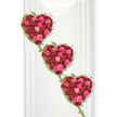 This image shows three rose-filled hearts arranged in a soft diagonal line, creating a graceful, romantic funeral tribute that seems to flow gently from top left to bottom right. Each heart is meticulously shaped and fully covered in roses, leaving no empty spaces, so the surface looks plush and abundant. The colour scheme centres on deep red roses, rich and velvety, mingled with vivid pink and tender blush blooms, forming a sophisticated blend of passion, affection, and tenderness. The roses themselves show different stages of bloom: some tight, promising buds hint at memories held close, while larger, open blossoms reveal many folded petals, like layers of shared stories and experiences. Around the edges of each heart, slim threads of ivy curl and loop, their small green leaves adding freshness and giving the hearts a defined outline. These vines also link the hearts to one another, forming subtle connections that convey the sense of a family tribute or a set of hearts representing loved ones bound together. The background is bright white and smooth, reminiscent of the walls in a peaceful Queensbury chapel or a modern memorial space near the station, allowing the reds, pinks, and greens to stand out in sharp, respectful contrast. Gentle, even lighting highlights the texture of every petal and the natural gloss of the foliage without casting strong shadows, which lends the scene a calm, contemplative atmosphere. This design feels especially appropriate for a funeral, memorial, or celebration of life in Queensbury, a floral expression crafted to say a profound, beautiful goodbye.