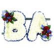 A quietly solemn and meticulously constructed floral tribute shapes the capital letters B and A, presented side by side against a clean white background. Each letter is formed from a dense, pillowy carpet of small, pristine white chrysanthemum blooms, their layered petals catching soft light to create a gentle, almost luminous texture. The crisp contours of both letters are defined by a rich royal blue satin ribbon that has been carefully wrapped and ruffled along the edges, giving a formal frame to the cloud-like white surface. On the upper left curve of the B and the lower right stroke of the A sit two matching accent clusters: velvety deep red roses in mixed stages from tight bud to half-open, paired with electric blue delphinium sprays that add vertical punctuation and cool contrast. Dark green leaves and pale green trailing tendrils weave through the accents, softening the geometry and lending a subtle sense of movement. The pair rests securely on a narrow dark green base that keeps the display freestanding and level, a detail often requested for chapel or crematorium placement. The overall effect is one of respectful clarity - purity in the white chrysanthemums, warmth and love in the red roses, and a composed dignity in the royal blue ribbon and blue delphiniums. Families in Queensbury and neighbouring Kingsbury or Wembley will recognise this as a traditional, personalised memorial initial tribute, a floral message crafted to read both visually and emotionally for a service or commemorative display, where colour, texture and placement speak of remembrance and care.