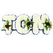 A bespoke funeral flower tribute in the form of the name TOM is shown here, crafted as three separate, three-dimensional letters aligned in a neat row. Each letter is built on a sturdy frame and completely covered with tight clusters of white chrysanthemums, giving a uniform, cushion-like effect that feels gentle and serene. Along the perimeter of every block capital runs a sleek royal blue ribbon, pleated and pinned to create a crisp edge that sharply outlines the contours of the T, O, and M, making the name clearly legible even from a distance at a chapel or graveside service in Queensbury. Carefully placed on the upper left of the 'T', at the outer curve of the 'O', and near the top right of the 'M' are small floral sprays that break the white surface with rich colour. These comprise deep, velvety red roses, smaller white or cream spray roses, and slim white blooms that recall freesia, nestled among a mix of green foliage, including delicate fern fronds and fuller leaves. The interplay of white, red, blue, and green gives the arrangement both structure and emotional warmth, suggesting purity, remembrance, respect, and lasting affection for a loved one named Tom. The letters are mounted on a dark rail, suggesting a freestanding display ready for placement on a stand or coffin top at local services, from quiet church ceremonies to crematorium farewells. The entire tribute feels calm, dignified, and deeply personal, like something a family in Queensbury might choose when they wish their funeral flowers to speak clearly of love and gratitude.