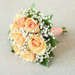 There's a quiet magic in this hand-tied bouquet: creamy peach roses gathered close and surrounded by a froth of white gypsophila, as though someone has captured the very first tender moment of spring. The roses glow with a soft, buttery peach that reflects a gentle, cool light; their petals feel velvety beneath the fingertips and suggest a faint, familiar fragrance that evokes fresh linen and early sunlight. Nestled among the blooms, delicate sprays of baby's breath form a translucent border, each tiny white blossom contributing to an impression of innocence and wonder. Dark, glossy foliage anchors the arrangement, the leaves' smooth surfaces and emerald depth giving the flowers contrast and presence. The stems are wrapped in peach satin ribbon, finished by a string of small pearls - a classic, tactile detail that offers both comfort in the grip and a refined nod to tradition. As a florist who arranges bouquets for couples marrying near Queensbury High Street, Roe Green Park, or small local chapels, I imagine this bouquet in a bride's hands as she steps into soft light; it breathes an understated, celebratory joy that suits weddings, intimate ceremonies, or elegant table décor. The design feels balanced, fragrant, and luminous - an emblem of hopeful beginnings rendered with careful artistry and a gentle, romantic spirit that feels utterly local and warmly familiar.