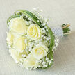 An elegant, classic bridal bouquet resting on pale beige linen, composed of seven generous creamy-white roses that read as a soft, luminous focal point. Each rose is artfully staged-some fully unfurled, others still cupped-to create a rhythm of texture and depth, while clusters of tiny, snow-white gypsophila float between the larger blooms, lending an ethereal, cloudlike softness. Loops of glossy green foliage, likely bear grass, are threaded around the bouquet's perimeter; their long, arcing lines provide a contemporary contrast to the rounded roses and guide the eye around the composition. The stems are neatly gathered into a firm yet comfortable handle and finished with a silvery-white satin ribbon, edged and trimmed with delicate pearled beads that reflect the ambient light with a pearlescent gleam. The bouquet is photographed diagonally against a neutral, finely textured fabric, the lighting soft and even to emphasize petal detail, the satin sheen, and the gentle shadowing that gives the arrangement its three-dimensional warmth. There is a faint suggestion of fresh rose scent and the cool, satiny feel of the wrapped stems-details that speak of careful craftsmanship. Prepared and available for local delivery across Queensbury and neighbouring Harrow and Kingsbury, this bouquet carries an air of understated luxury suited for weddings, anniversaries, or an intimate ceremony at a local community hall. Flower Delivery Queensbury creates this composition with an eye for balance, comfort, and the quiet joy that a simple palette of cream and green can convey.
