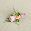 Laid gently on a piece of woven, lightly textured fabric, this elegant boutonniere looks ready to be pinned to a lapel before a celebration in Queensbury. At its centre, a cool pink rose unfurls in soft spirals, its outer petals thin and almost see-through, catching the light in a way that makes the bloom appear freshly misted. Surrounding it, pastel alstroemeria blossoms cup the rose with painterly grace, their blush-pink petals edged delicately and opening to reveal warm yellow throats with subtle speckles. Small sprays of white gypsophila peek between the larger flowers, like tiny stars scattered across a dusk sky over Stag Lane, softening the composition and adding romance. Fine, featherlike greenery arcs and twists, providing contrast with its crisp texture and rich green hue, framing the flowers without overwhelming them. The stems have been bound with a precise wrap of satin-finish pink ribbon, smooth and glossy, forming a neat, tapered handle that sits comfortably between finger and thumb. Light falls gently from one side, creating mild shadows that highlight the layers of petals and the thoughtful structure of the piece. You can almost feel the cool, velvety rose, the slightly firmer alstroemeria, and the airy touch of the baby's breath as you imagine holding it. This boutonniere suits a groom, best man, or prom guest heading out from a Queensbury home or venue, its quiet style speaking of care, tenderness, and the timeless symbolism of soft pink flowers worn close to the heart.