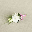 Resting on a softly textured, light-coloured fabric, this boutonniere captures a moment of quiet romance, as if it has just been set down in a calm studio off the streets of Queensbury. At the centre sits a luminous white lisianthus bloom, its petals layered and slightly ruffled, giving an impression of silk gently stirred by a breeze. The white is not stark but creamy, with a warmth that feels welcoming, like afternoon light slanting across a local garden. Flanking the main flower are two slender lisianthus buds, their tips still closed, offering a sense of unfolding stories and new beginnings. Sprinkled among them, tiny white blossoms of baby's breath float like soft whispers, creating a delicate, cloudlike veil around the focal bloom. Slender, reedy greenery stretches and curves along the composition, providing contrast and movement, as though the boutonniere had just been picked from a well-tended Queensbury allotment. The stems are bound in a glossy, bright pink satin ribbon that wraps snugly from top to bottom, its vivid colour and smooth shine adding a subtle, joyful energy. A neatly tied bow sits at the base, crisp and balanced, mirroring the careful attention of an experienced florist used to preparing wedding flowers for local venues. The neutral woven backdrop emphasises every nuance of texture-the smooth ribbon, the feather-light gypsophila, the velvety lisianthus petals-resulting in an arrangement that feels both polished and intimate, ideal for weddings, proms, or any milestone day celebrated around Queensbury.
