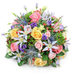 Photographed against a clean white backdrop, this abundant, rounded bouquet looks like a snapshot of a well-tended garden, gathered at just the right moment and shaped into a generous dome. The arrangement is tightly composed yet never stiff, with each bloom nestled closely to the next, creating a sense of fullness and quiet luxury that would suit a cosy home in Queensbury or a small gathering near Canons Park. At its heart, plush garden roses in gentle pinks, soft peaches, and warm yellows unfurl in spiralling layers, some open and inviting, others still partially wrapped in their outer petals. Fine veils of clematis weave through in white and pale lavender, their star-like petals and soft yellow centres adding a light, airy movement through the design. Contrasting with this delicacy, bold stems of blue Eryngium stand out, their spiky, steel-blue heads lending an intriguing, slightly wild texture that keeps the bouquet from feeling overly traditional. Around and between the roses, rich purple lisianthus blossoms provide a deeper tone, their ruffled petals and curling buds adding to the sense of depth. Here and there, bright red Hypericum berries appear like tiny, polished beads, offering flashes of colour and a playful counterpoint to the soft petals. A layered collar of greenery in varied shades of green, from sleek broad leaves to fine, feathery foliage and hints of darker, wine-tinged leaves, gives the bouquet structure and a natural, garden-bed feel. The overall impression is one of thoughtful craftsmanship and quiet celebration, the kind of bouquet chosen to send warm wishes across Queensbury, whether for a birthday, a get-well message, or simply to bring a little burst of floral joy indoors.