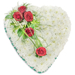 Large heart-shaped funeral tribute composed entirely of white and red flowers, photographed against a plain white backdrop to highlight every contour. The heart is fully massed with small, pristine white chrysanthemum heads, each bloom tightly packed to create a plush, cushion-like effect that suggests softness, purity, and serenity. At the upper left curve, three luxurious deep red roses form a striking spray, their petals layered in tight spirals and glowing warmly against the cool white base. Around them, a delicate collection of white filler flowers and assorted greenery-glossy leaves, fine ferny fronds, and airy stems-adds texture and natural movement, preventing the design from feeling too formal or static. Two more red roses are placed further down on the right side of the heart, supporting a gentle diagonal line through the arrangement. These roses are linked visually to the main cluster by slim, arching blades of vivid green decorative grass that sweep across the chrysanthemums, echoing the contours of the heart and suggesting a sense of continuity and connection. A thin, dark green satin ribbon trims the entire outer edge, its subtle sheen providing a polished, professional finish that frames the flowers beautifully. The overall feel is dignified and comforting, a classic red and white heart that would be chosen by families in Queensbury to honour a loved one at a funeral, memorial, or graveside ceremony, conveying both grief and deep, unwavering affection.