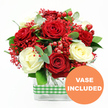 A lush bouquet of red and white roses is displayed against a bright white background, giving the impression of fresh flowers just delivered to a doorstep in Queensbury. The arrangement is dominated by sumptuous, fully opened red roses, their velvety petals layered in soft, romantic spirals that immediately catch the eye. Nestled among them, creamy white roses unfold in smoother, more rounded blooms, their gentle tones bringing balance and a sense of calm elegance to the vibrant reds. Between the larger flowers, sprays of minute red filler blossoms, much like dyed gypsophila, stretch in feathery clusters, filling the spaces with a mist of colour that suggests delicate movement. Scattered throughout, glossy red hypericum berries form small, rounded bunches that stand out with their polished shine, adding a bright, celebratory accent that feels perfect for winter gatherings or summer parties alike. The bouquet is supported by a base of rich green foliage; smooth, deep green leaves and slender, slightly bluish eucalyptus sprigs create layers of texture and shape, as though they were selected from local gardens near Queensbury Park. All the stems sit neatly inside a rectangular clear glass vase, its transparent sides revealing the submerged stems and clean water within. Around the centre of the vase, a green and white gingham ribbon wraps horizontally, its checked pattern lending a cosy, rustic charm that calls to mind relaxed kitchen tables and family celebrations. In the lower right corner of the image, an orange circular badge with clear white lettering states VASE INCLUDED, making it evident that this is a complete, ready-to-display floral gift-ideal for birthdays, anniversaries, or a spontaneous gesture to brighten someone's day in Queensbury.