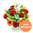 This image shows a joyful, densely packed floral arrangement photographed against a completely white background, every stem and petal clearly defined as if freshly arranged by a local Queensbury florist. The flowers sit in a modern, rectangular clear glass vase, which allows the viewer to see the straight green stems gathered neatly together, while a light green and white gingham ribbon wrapped low around the vase lends a charming, homely accent that would suit a dining table in a flat off Honeypot Lane or a sunny windowsill near Queensbury Circle. At the heart of the bouquet, velvety deep red roses and red-orange carnations form a rich, warm centre, their layered and ruffled petals suggesting fullness and abundance. Surrounding them, bright orange gerbera daisies extend their flat, daisy-like petals around dark central disks, radiating an almost sunburst energy that animates the arrangement. Between these larger heads, small, spherical lime-green pompom chrysanthemums peep out, adding a lively, contemporary contrast and soft, cushion-like texture. Elegant white Oriental lilies rise above the main cluster, some fully open with soft pink streaks along their inner petals and prominent stamens, others poised in bud, offering a promise of fragrance and unfolding beauty over time. The entire composition is framed by a mix of lush, glossy dark green leaves and airy silver-green eucalyptus, whose slender, rounded leaves arc gently outward, creating an attractive silhouette reminiscent of a thoughtfully tended garden. In the bottom right corner of the photograph, an orange circular graphic overlaps the vase, with bold white capital letters stating VASE INCLUDED, clearly signalling that this stylish glass container is part of the arrangement and ready to display the moment it arrives in a Queensbury home or workplace.