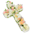 A substantial floral cross, designed as a tender sympathy tribute, is shown against a pristine white background where every bloom is clearly visible. The cross shape is immediately recognisable, its lines softened by a dense covering of fresh flowers that create a cushioned, almost velvety effect. The foundation of the piece is made up of tightly clustered white and cream-toned flowers: large roses with gently curling petals, smaller spray roses for added detail, and plush white hydrangea or similar full-headed blooms that fill the structure with volume. This serene white base is warmed by gentle pastel accents. Throughout the cross, you can see clusters of soft peach and apricot roses, along with delicate light pink blooms that appear in varying stages of opening, from budding to fully blossomed. These colours lend the design an understated warmth, like a soft spoken word of comfort. Tiny hints of lavender or pale purple filler flowers are interspersed between the petals, adding a fine, almost lace-like texture and a graceful touch of contrast. Along the edges of the cross and tucked discreetly among the flowers, small sprigs of fresh greenery emerge, outlining the shape and adding depth. The overall impression is one of peaceful elegance and careful craftsmanship, reminiscent of a lovingly prepared funeral tribute created for a family in Queensbury, perhaps for a service at a local church or crematorium. The arrangement speaks of faith, remembrance, and the hope of eternal rest, offering a gentle visual embrace to those gathered to say their goodbyes.