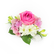A compact, thoughtfully arranged corsage sits on a pristine white background, rendered with the kind of careful attention a local Queensbury florist would use for a special occasion. At the centre, a plush bubblegum-fuchsia rose opens in concentric layers of velvety petals, each inner curl gradually loosening into a fuller bloom that radiates a warm, romantic tone. Nestled around it are clusters of soft pastel hydrangea in shades of pale pink and a gentle lavender-pink, their tiny florets building a cushion of airy volume and tender texture. Two creamy white, trumpet-shaped blooms-suggestive of small lilies or alstroemeria-tilt outward beneath the rose, their green-tinged throats introducing a cool contrast and a whisper of purity. Glossy deep-green leaves fan from the base, broad and reassuring, anchoring the composition with the fresh scent of cut foliage, while slim green buds edged in yellow reach upward like promises of more blooms to come. At the bottom right a small cluster of luminous white pearls is woven in, the soft sheen and slight variance in bead size lending an heirloom quality that pairs beautifully with wedding attire or formal evening wear. Soft, natural light washes the scene, revealing petal textures from satiny to slightly papery and suggesting the gentle perfume of roses and summer hydrangeas. This piece feels intimate and poised-ideal as a bridal corsage, prom accessory, or anniversary keepsake for couples gathering near Queensbury Tube, Kingsbury High Road, or Roe Green Park-crafted with the kind of composure and freshness neighbours expect from their local florists.