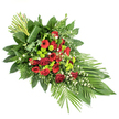 A gracefully tapered sympathy spray lies across a plain white background, its elongated form suggesting a gentle bow or farewell, well suited to a funeral or memorial gathering in Queensbury. Deep red blooms form the emotional core: roses in various stages of opening, from tight buds to full, velvety rosettes, sit beside open-faced gerbera daisies with darker centres and layered red carnations whose soft, ruffled petals create a feeling of fullness and tenderness. Interspersed between these commanding reds, clusters of apple-lime green button chrysanthemums create bright, rounded pops of colour that lift the arrangement, offering a note of renewal amidst the solemn tones. Delicate white filler flowers, perhaps small daisies or airy gypsophila, weave gently through the composition, catching the light and softening the transitions between flowers. A rich collection of greenery frames the spray: broad, glossy leaves such as salal or ruscus provide a solid, dark green base, while feathery ferns and slender palm-like fronds stretch outward, particularly along the lower right edge, echoing the movement of leaves in the breeze across Queensbury's residential gardens. At the top left, a small cluster of long, straight green stems rises upright, their base encircled by a single broad leaf that wraps around them in an elegant, contemporary flourish. The overall effect is one of calm dignity and thoughtful craftsmanship, a floral tribute designed to rest atop a casket or be displayed as a standing spray, conveying love, respect, and remembrance to family and friends gathered to say goodbye.