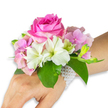 A delicate wrist corsage rests against a clear white backdrop, presented on a left hand and forearm with a light-to-medium skin tone so the flowers read with bright clarity. At the centre sits a fully opened, deep fuchsia-pink rose whose tightly layered petals form a plush spiral, offering both visual depth and the suggestion of a gentle, honeyed scent. Surrounding the rose are clusters of soft blush-pink hydrangea florets that lend a cloudlike texture and diffuse the composition with pastel volume; their tiny, papery petals catch soft studio light and seem almost translucent at the edges. Scattered among the hydrangea are pristine white alstroemeria-Peruvian lilies-each sporting four to six smooth petals and faint pale green brushstrokes at their throats, a refined detail that brightens the arrangement. To the right, a small spray of pale green alstroemeria buds and a few barely opened pink buds promise future bloom and add a sense of tender anticipation. Broad, glossy emerald green leaves cradle the flowers, their rich colour creating a fresh, verdant frame that lifts the pinks and whites forward. The arrangement is fastened by an elegant multi-strand bracelet of tiny, lustrous white pearls that loop around the wrist and trail delicately toward the back of the hand, providing a classic, wearable finish. The overall mood is poised and gently romantic-ideal for prom, a first dance, or a bridal party touch-and the craftsmanship reflects the careful hand of a neighbourhood florist who understands balance, texture, and wearable comfort in Queensbury.