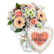 Captured against a plain white studio background, this Mother's Day arrangement feels bright, modern, and full of affection, like a thoughtful surprise waiting to be delivered across Queensbury. At the centre stands a clear glass vase with a softly rounded shape, its neck cinched by a simple band of rustic twine that adds a handmade, local-florist touch. The vase holds a generous, dome-shaped bouquet of mixed flowers in gentle pastel tones. Several peach-pink roses are fully open, their layered petals spiralling outward in graceful curves, with hints of warm apricot near the centres. Alongside them, bold peach gerbera daisies with deep brown or almost black centres create a striking focal point, their daisy-like faces radiating cheerful energy. Threaded throughout the design are delicate white sprays of baby's breath, so fine they resemble tiny stars or flecks of lace, and smaller white chrysanthemums whose pale green hearts bring a subtle freshness. Lush green foliage frames the flowers, giving the arrangement structure and a garden-fresh feel, as though the stems were gathered that morning from nearby Queensbury gardens. Slightly behind the bouquet, a small white greeting card nestles, its colourful lettering largely hidden but clearly celebratory. In the foreground to the right, a large heart-shaped foil balloon leans in, sharing the spotlight. The balloon's white surface is scattered with shiny gold and silver dots, like confetti mid-flight, and at its centre sits a peach-coloured heart. Inside this heart, the words HAPPY Mother's DAY appear in bold black lettering, with the word Mother's written in flowing script. The entire scene radiates gratitude, tenderness, and the joy of honouring mums in Queensbury with flowers and a keepsake balloon.