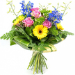 A joyful hand-tied bouquet is pictured standing upright against a clean white backdrop, its vivid colours appearing even more intense in the simple setting. In the centre, soft pink roses open into generous spirals of petals, giving off an air of gentle romance and comfort that would suit anything from a birthday surprise to a thank-you gift in Queensbury. Around them, bright yellow gerbera daisies, each with a deep chocolate-brown centre, provide a bold, sunny contrast, their flat, radiating petals adding a modern graphic touch. Reaching above this warm central cluster, tall stems of rich blue delphinium or larkspur lift the eye upwards, the many small blooms along each stem creating a sense of vertical movement and cool elegance. The bouquet is surrounded and supported by a wealth of greenery: fine, feathery fern fronds soften the outline, while compact tufts of vivid green filler flowers and mossy textures fill in the gaps, giving the arrangement a full, abundant look. Broad, glossy leaves, some delicately striped with lighter green, are meticulously wrapped around the lower section of the flower heads, forming a smooth collar that frames the bouquet like a natural cuff. A few slender, pale green stems with tiny buds stretch lightly above the main flowers, conveying freshness, as though the bouquet has just been gathered from a garden near Queensbury Park or along Church Lane. The natural stems at the bottom are visible and neatly tied, emphasising the handcrafted nature of the design and making it an inviting choice for same-day flower delivery to homes and businesses throughout Queensbury.